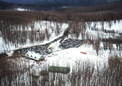 Aerial view of a ski resort with buildings, a crowded parking lot, and snow-covered trees.