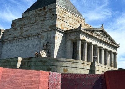 Stone memorial with pyramid roof and columns, red modern entrance in foreground.