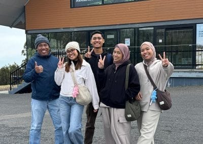 Five smiling friends pose in front of the Lake Mountain building.