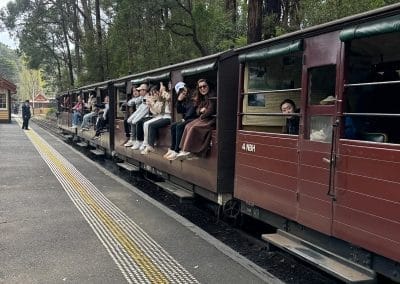 Red tourist train passing through a forest with seated passengers