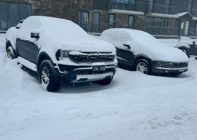 Snow-covered pickup truck and car in a parking lot.