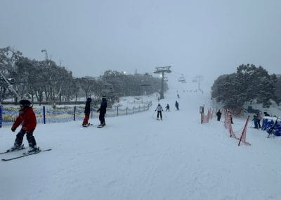 Skiers on a snowy slope with chairlifts and trees in the background.