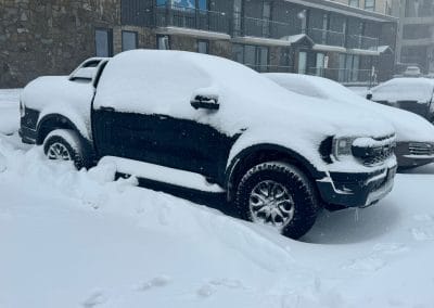 Snow-covered pickup truck and car in a parking lot.