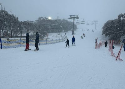 Skiers on a snowy slope with chairlifts and trees in the background.