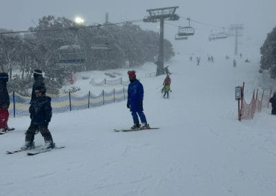 Skiers on a snowy slope with chairlifts and trees in the background.