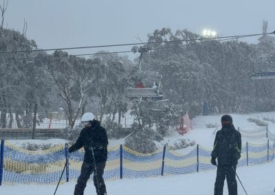Skiers on a snowy slope with chairlifts and trees in the background.