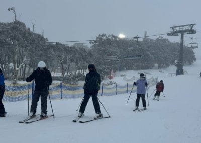 Skiers on a snowy slope with chairlifts and trees in the background.